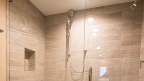 A modern bathroom with a glass-enclosed shower, a toilet, and a small shelf with a towel.