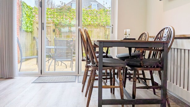 A dining area with a table and chairs, a sliding glass door leading to a garden, and a television mounted on the wall. - Pears Grove - Southbourne - a family house that sleeps 6 guests in 3 bedrooms (Emsworth)