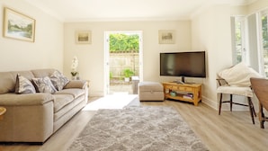 A living room with a sofa, a TV, a wooden coffee table, and a chair. There is a door leading to a garden. - Pears Grove - Southbourne - a family house that sleeps 6 guests in 3 bedrooms (Emsworth)