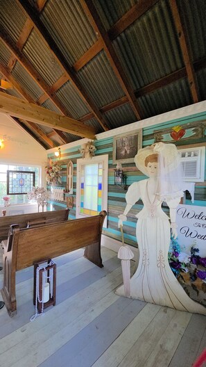Ein rustikaler Innenraum mit einer Holzbank, einer Wand mit Herzmotiv und einem Schild mit der Aufschrift 'Welcome to Wedding'.