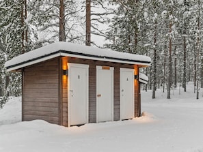 Une petite cabane en bois avec deux portes, l’une portant l’inscription « B » et l’autre « A », située dans une forêt enneigée.