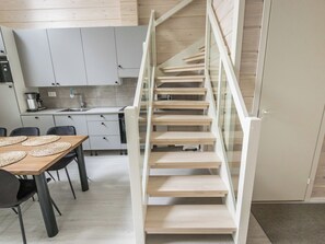 A modern kitchen with white cabinets, a dining table with placemats, and a wooden staircase with glass railings.