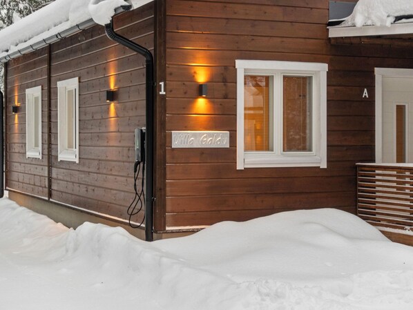 Une cabane en bois avec une pancarte indiquant « Villa Goldu », un câble noir et une fenêtre avec des stores.