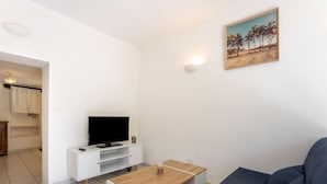 Un soggiorno moderno con una televisione a schermo piatto su un mobile bianco, un tavolino in legno e un divano blu scuro.