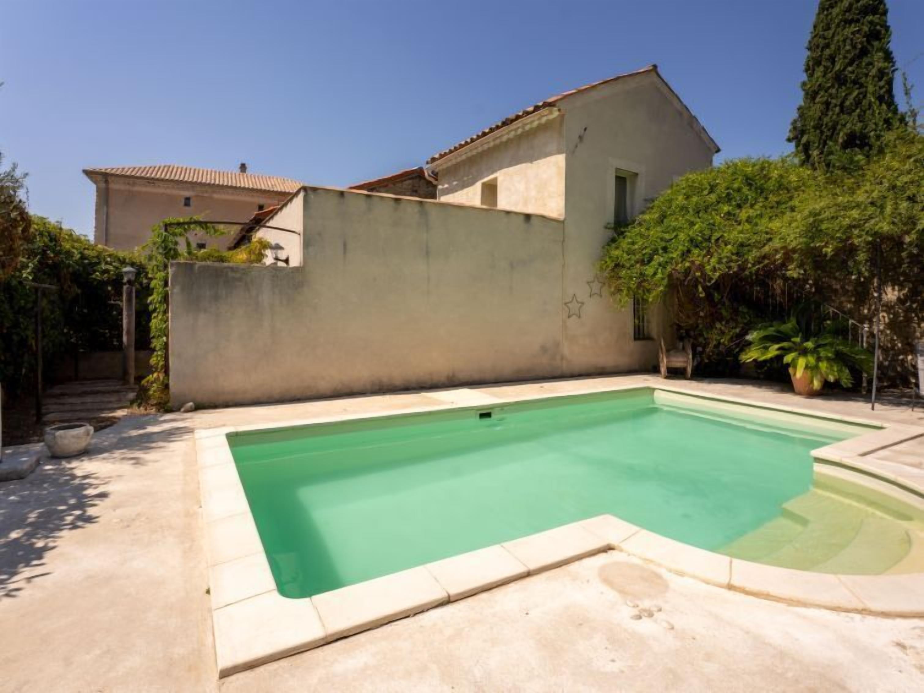 A swimming pool with a tiled deck, surrounded by a low wall and lush greenery.