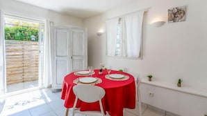 Zona pranzo con tovaglia rossa, sedie bianche e una finestra con tende bianche.