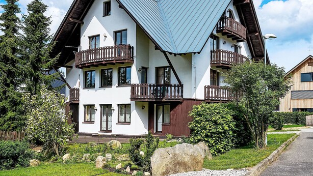 Eine zweistöckige Chalet mit steilem Dach, Holzbalkonen und einem gepflegten Garten.