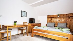 Une chambre avec un lit en bois, un bureau et une chaise. On y trouve également un téléviseur posé sur une commode en bois.