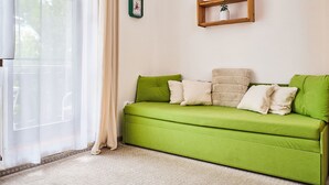 Un canapé vert agrémenté de plusieurs coussins, une étagère en bois avec une petite plante et une horloge murale.