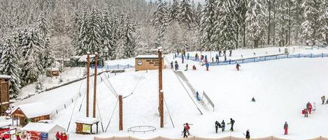 A snowy ski slope with a ski lift, trees, and skiers.