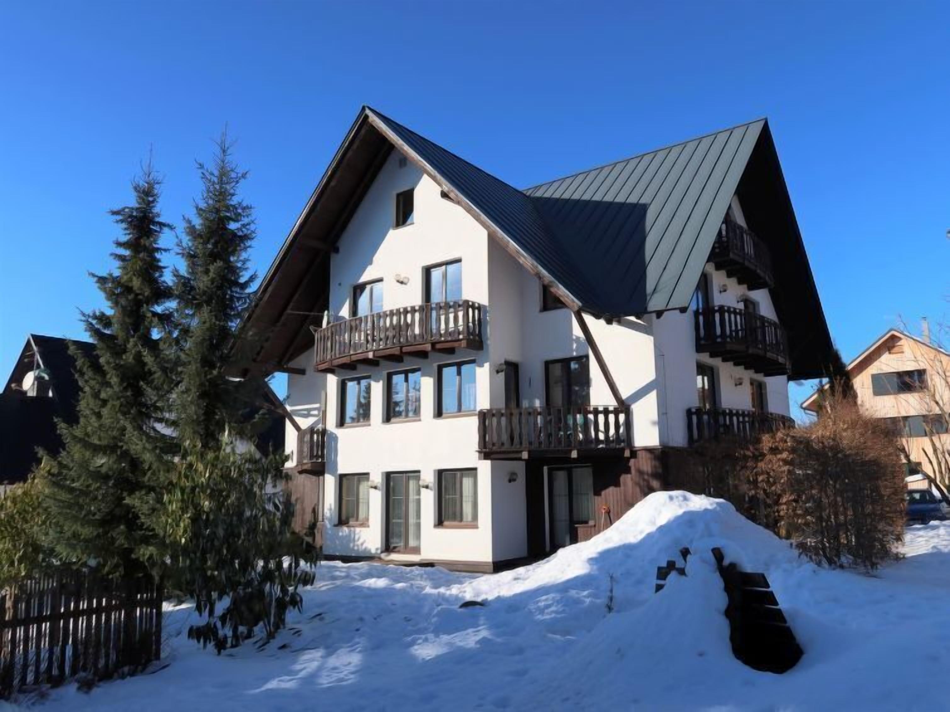 Un immeuble à plusieurs étages doté de balcons, entouré de neige et d’arbres.