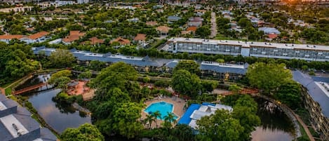 Un quartier résidentiel doté d’une piscine centrale, entourée de verdure et bordée d’un plan d’eau.