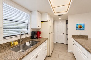 A modern kitchen with granite countertops, white cabinetry, a built-in oven, and a coffee maker.