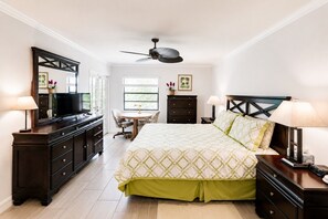 Une chambre à coucher comprenant un lit, une commode, un téléviseur, un bureau, une chaise et un ventilateur de plafond.