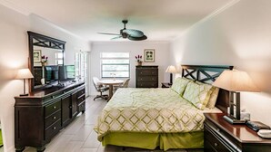 A bedroom with a bed, desk, dresser, and ceiling fan.