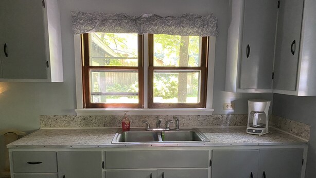 A kitchen with a double sink, a window with a lace valance, and a coffee maker on the countertop. - SPORTSMAN/COUPLES RETREAT. Close to Lakes, Rivers, & Beautiful Ludington (Custer)