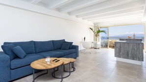 A modern living room with a blue sofa, two wooden tables, and a view of the sea.