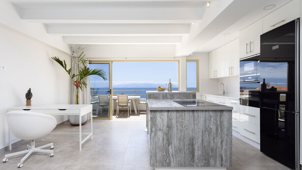 A modern kitchen with a large island, white cabinetry, and a view of the sea.