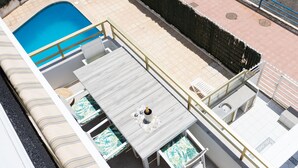 A rooftop pool area with a wooden deck, lounge chairs, and a small table with a bottle.