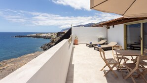 A balcony with a view of the sea, a table with chairs, and a potted plant.