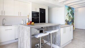 A modern kitchen with white cabinets, a built-in oven, and a bar area with stools.