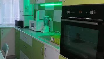 Una cocina con armarios verdes, un microondas, una licuadora y un horno.