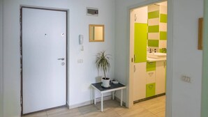 A hallway with a white door, a small table with a potted plant, a mirror, and a green and white tiled wall. - Stunning Green Studio 43 (Chiajna)