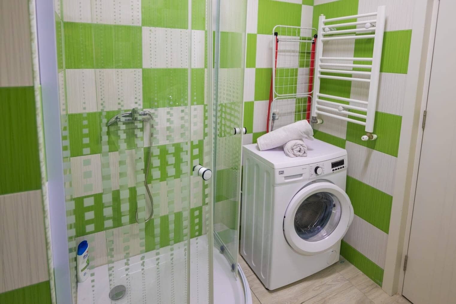 Un baño pequeño y de colores vivos con ducha, lavadora y un perchero para toallas.