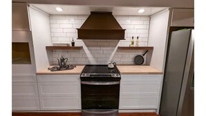 A compact kitchen with white cabinetry, a stainless steel stove, and a built-in oven. - English Cottage near Branson Attractions (Lampe)