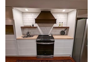 A compact kitchen with white cabinetry, a stainless steel stove, and a built-in oven. - English Cottage near Branson Attractions (Lampe)