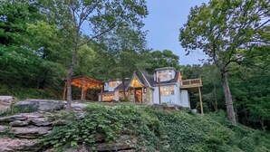 A rustic cabin with a stone foundation, surrounded by lush greenery and trees. - English Cottage near Branson Attractions (Lampe)
