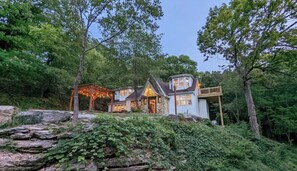 A rustic cabin with a stone foundation, surrounded by lush greenery and trees. - English Cottage near Branson Attractions (Lampe)
