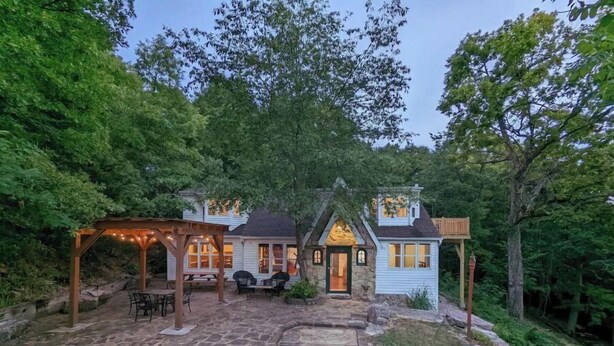 A two-story house with a stone patio, wooden pergola, and a stone pathway leading to the entrance. - English Cottage near Branson Attractions (Lampe)