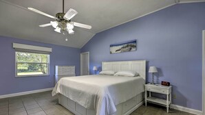 A bedroom with a bed, a nightstand, a ceiling fan, a window, and a wall clock.