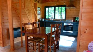 A wooden interior with a dining table and chairs, a kitchen with modern appliances, and a window with a view of greenery.