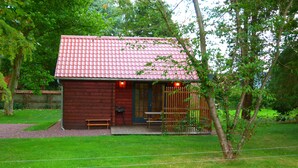 Une petite cabane rustique avec un toit recouvert de tuiles rouges, une véranda en bois et une cour clôturée.