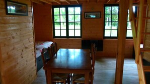 L’intérieur d’un chalet en bois comprend une table à manger, des chaises et deux fenêtres donnant sur un paysage verdoyant.