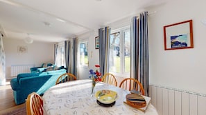 Une pièce comprenant une table à manger, des chaises, un canapé et une fenêtre avec des rideaux.