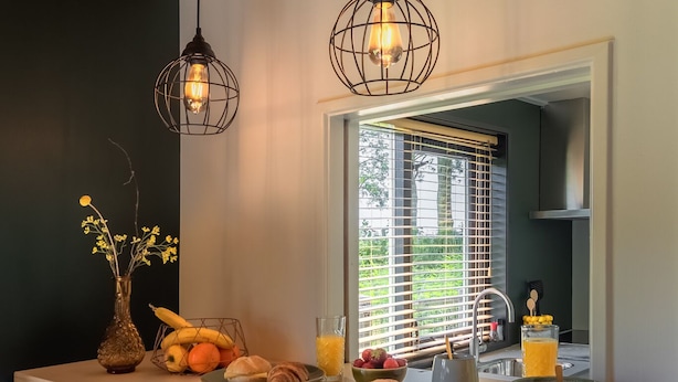 A breakfast bar with a mirror, two pendant lights, and a vase with flowers.
