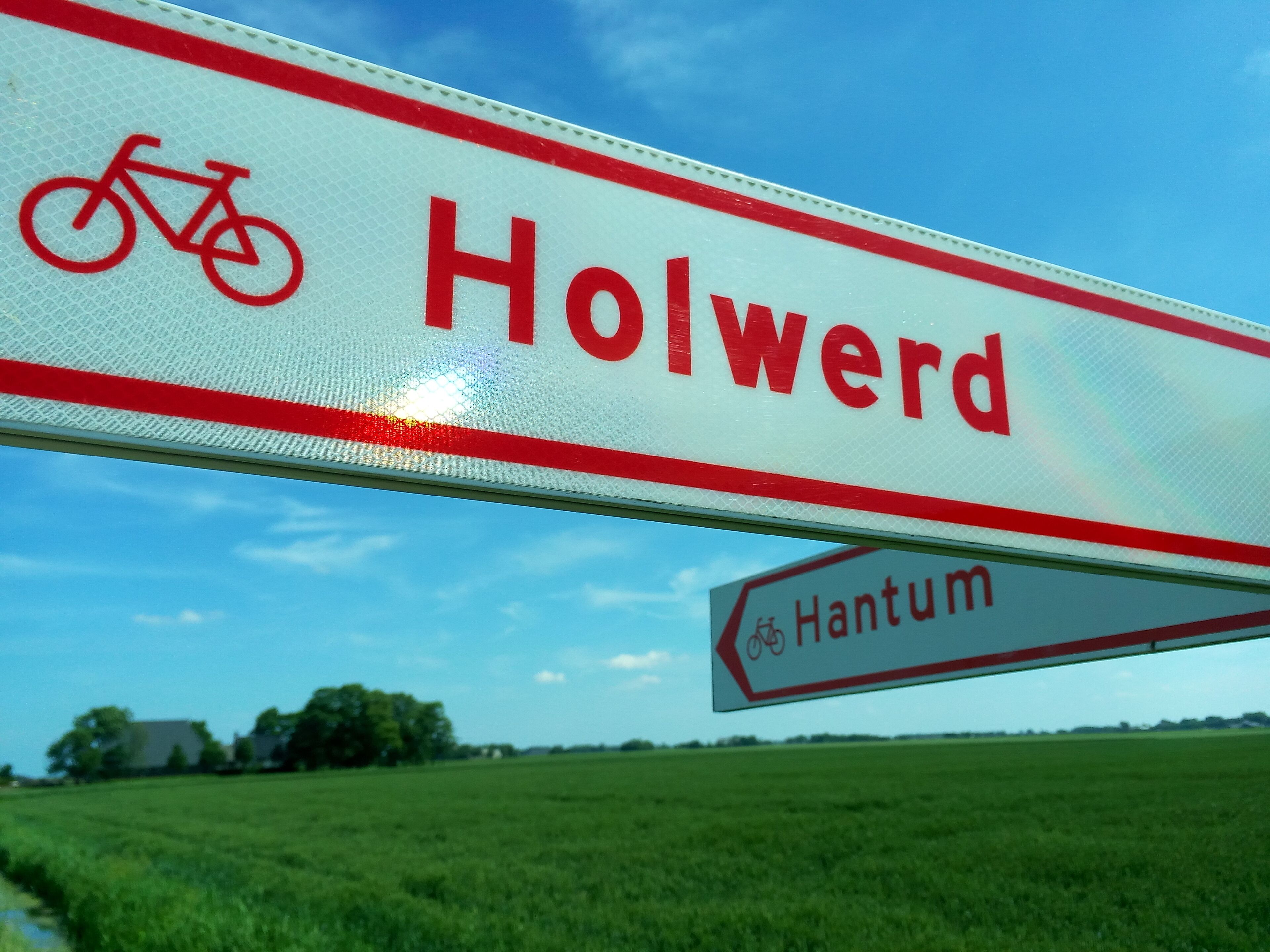 Un panneau de signalisation indiquant la direction de « Holwerd » et de « Hantum », et signalant un itinéraire cyclable.