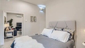A bedroom with a large bed, a headboard with a geometric pattern, and a small bedside table with a lamp.