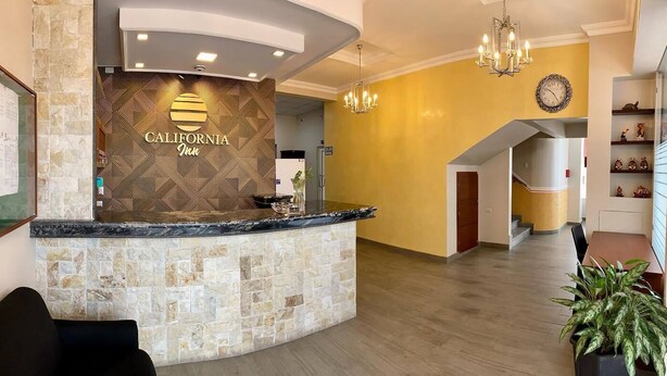 A reception area with a stone counter, a clock, and a yellow wall. - Hostal California Inn (Guayaquil)