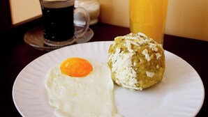 A plate with a fried egg and a pastry, a glass of orange juice, and a cup of black coffee on a table. - Hostal California Inn (Guayaquil)