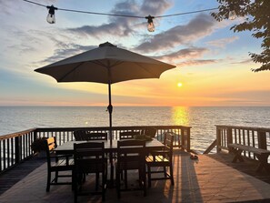 A wooden deck with a table and chairs, overlooking a body of water during sunset. - Lakefront Getaway at Renshaw Bay (Mannsville)
