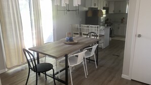 Een eetgedeelte met een houten tafel, witte stoelen en een keuken op de achtergrond.