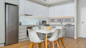 Eine moderne Küche mit weißen Schränken, einem Edelstahl-Kühlschrank, einem weißen Esstisch mit Stühlen und Holzboden.