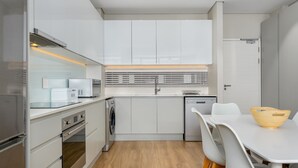Eine moderne Küche mit weißen Schränken, einem eingebauten Backofen und einem Essbereich mit weißem Tisch und Stühlen.