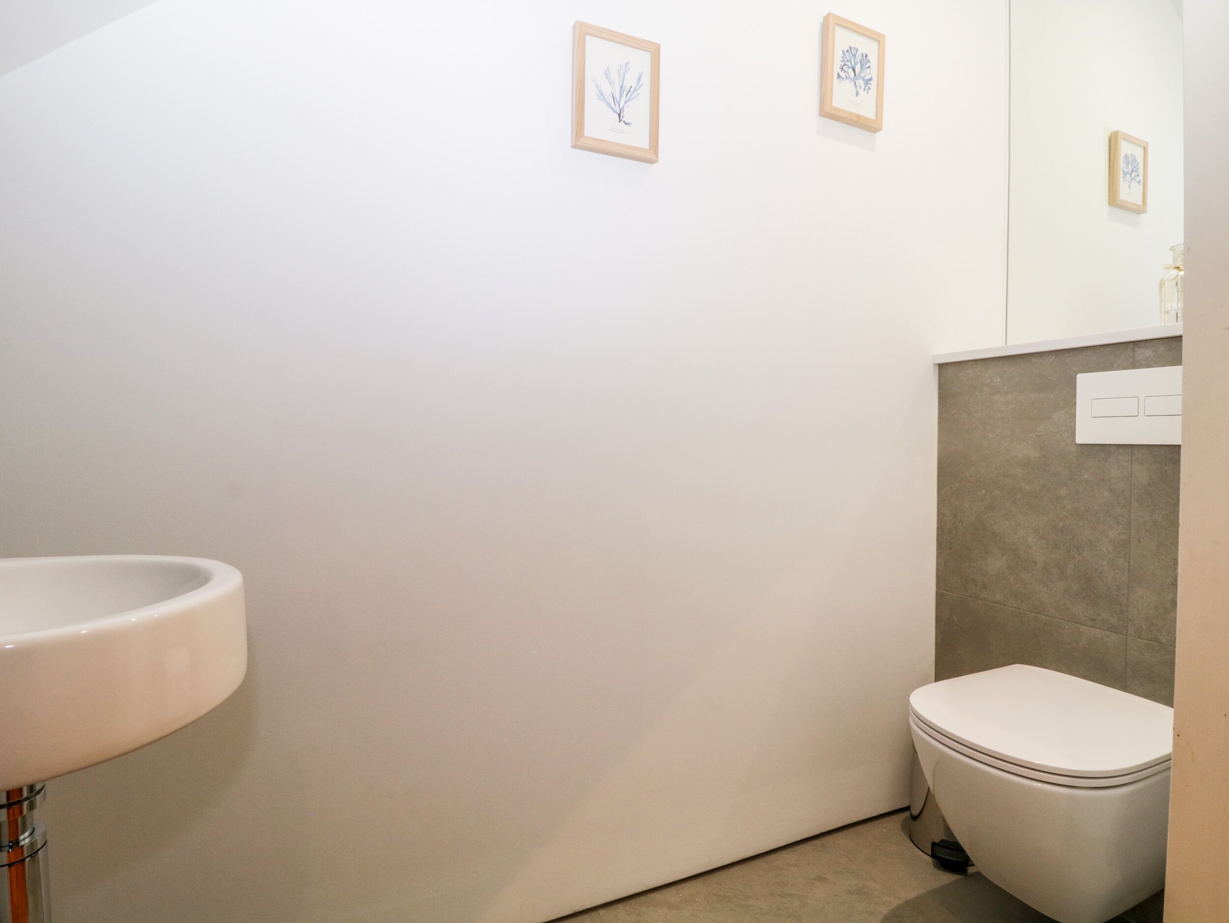 Un baño moderno con un lavabo, inodoro y pared de azulejos. Hay dos cuadros enmarcados en la pared.