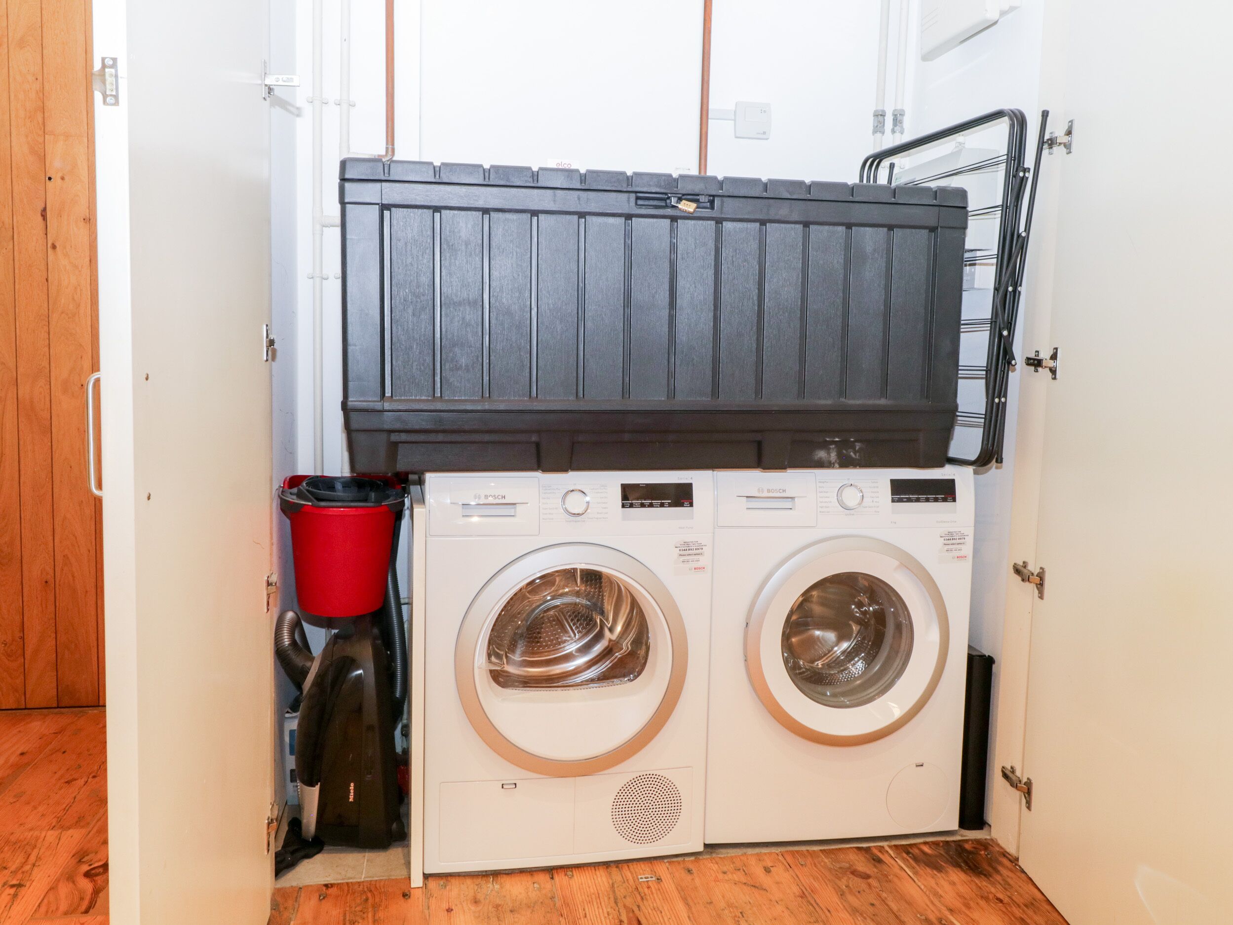 A laundry room with two front-loading washing machines, a red vacuum cleaner, and a black storage unit.
