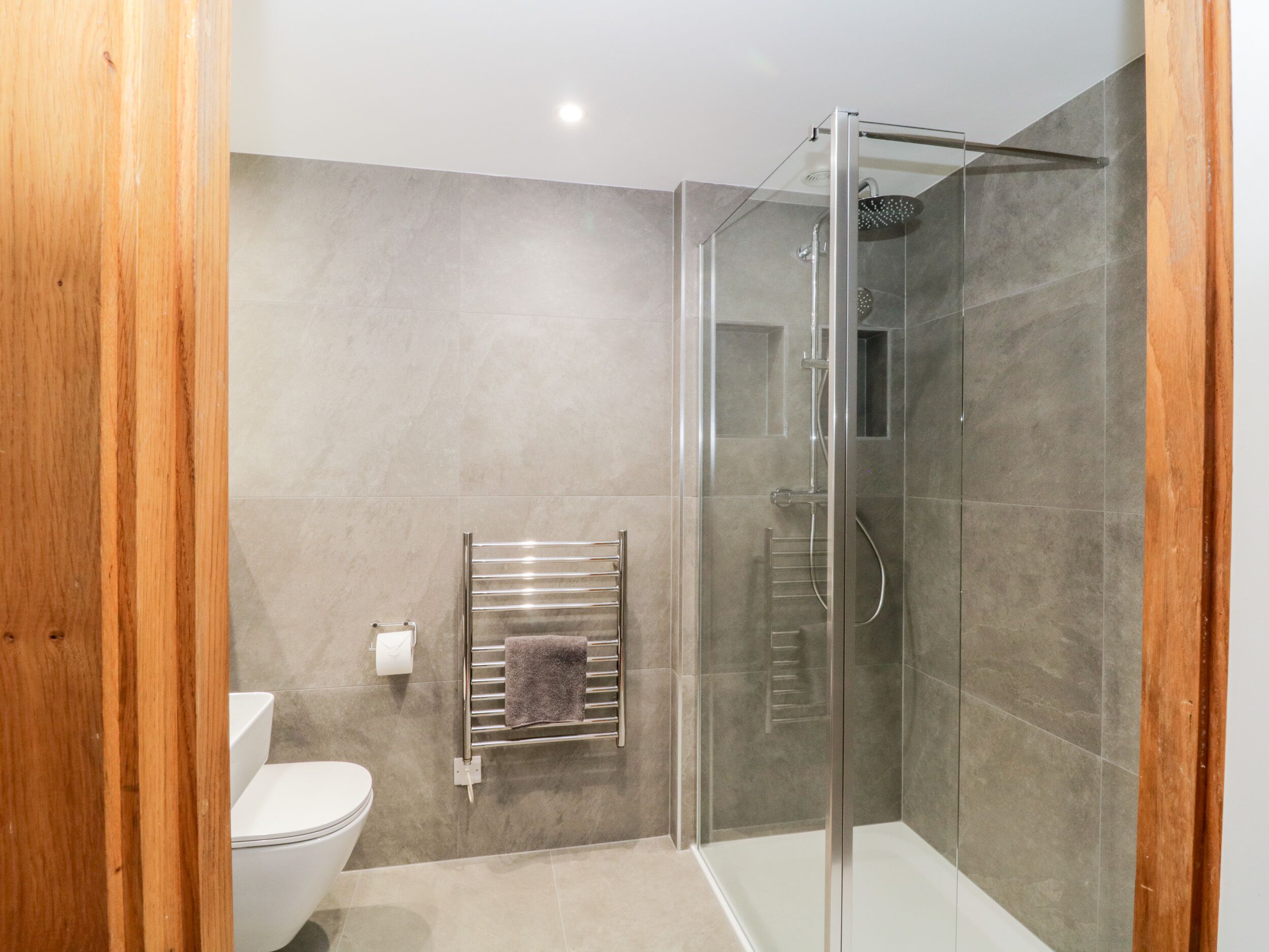 A modern bathroom with a glass-enclosed shower, a toilet, and a towel rack.